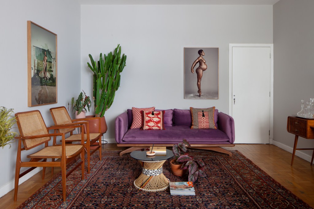 Mix de culturas no décor cria clima acolhedor em apê de 80 m². Projeto de Ricardo Abreu. Na foto, sala de estar com sofá roxo, fotos e tapete,
