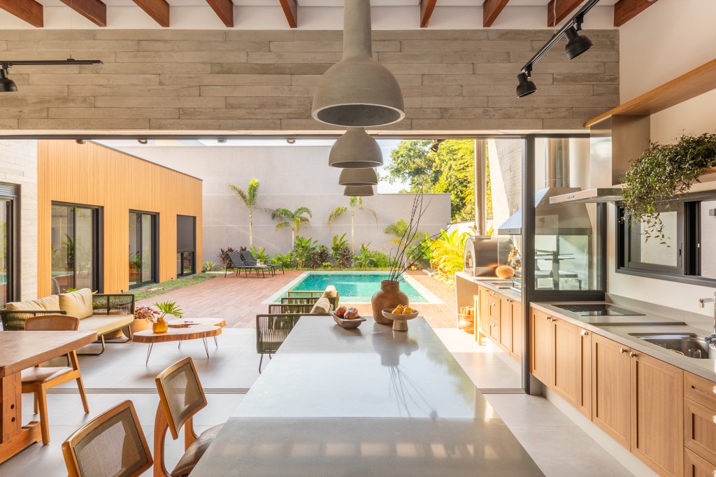 Pensada para veraneio, casa em meio ao verde vira o lar oficial da família. Projeto de Pietro Terlizzi. Na foto, cozinha com varanda, piscina e jardim.