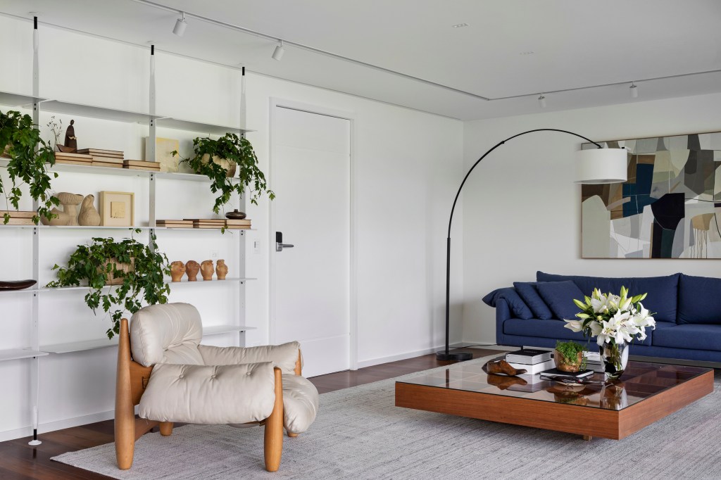 Com ampla varanda, apê de 200 m² tem décor inspirada no bairro do Leblon. Projeto de João Panaggio. Na foto, sala de estar com sofá azul e varanda com vista para as árvores.