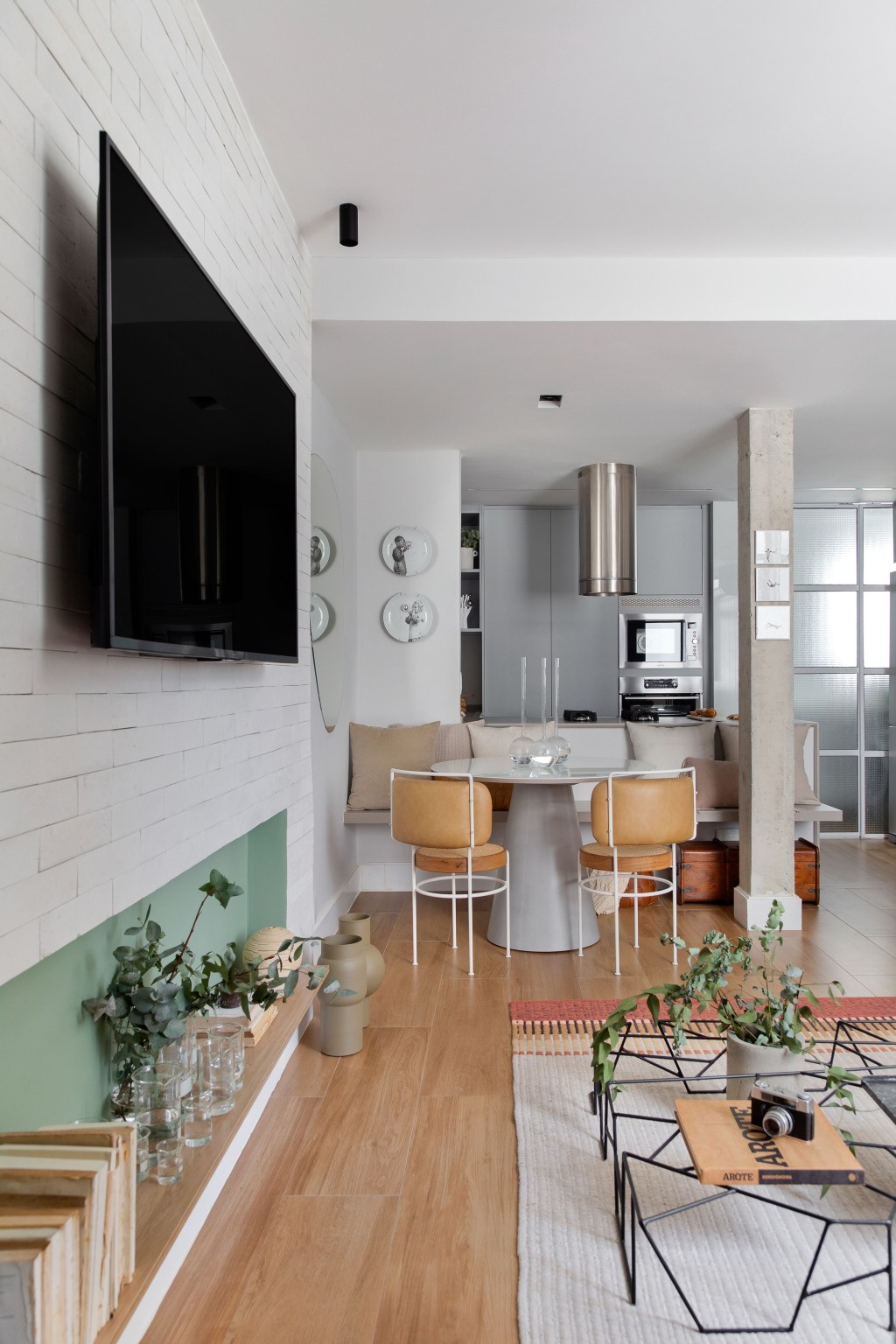 Apê de 60 m² ganha cozinha integrada, duas suítes e lavanderia escondida. Projeto de Sketchlab Arquitetura. Na foto, sala de jantar com mesa redonda e espelho orgânico.