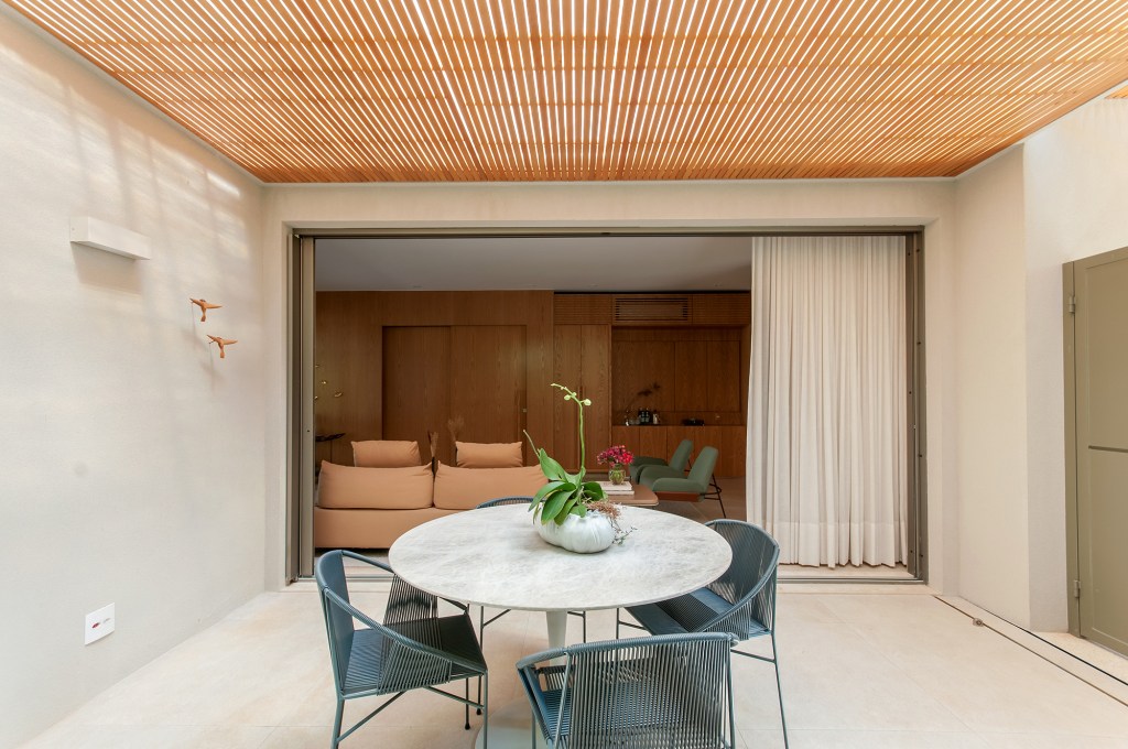 Construída do zero, casa une ambientes integrados e design nacional. Projeto de Paiva e Passarini Arquitetura. Na foto, varanda com teto ripado e mesa.