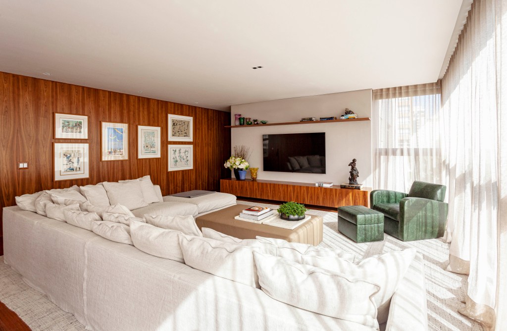 David Bastos assina apartamento clássico de 174 m² em São Paulo. Na foto, sala de TV com sofá em L, cortinas e poltrona verde.