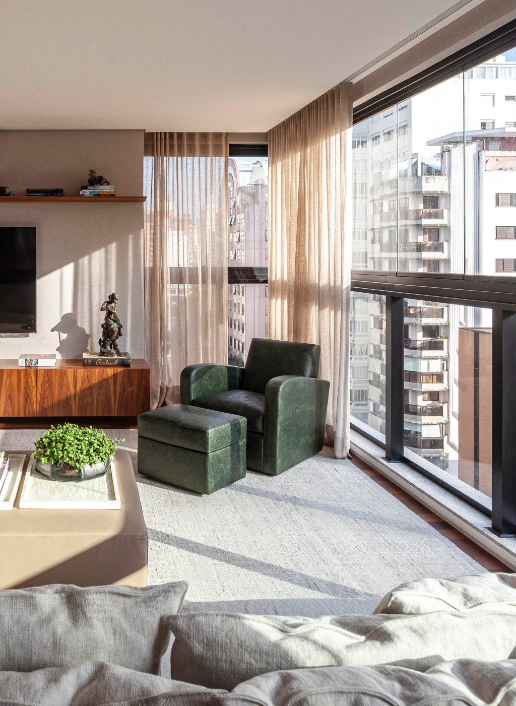 David Bastos assina apartamento clássico de 174 m² em São Paulo. Na foto, sala de TV com sofá em L, cortinas e poltrona verde.