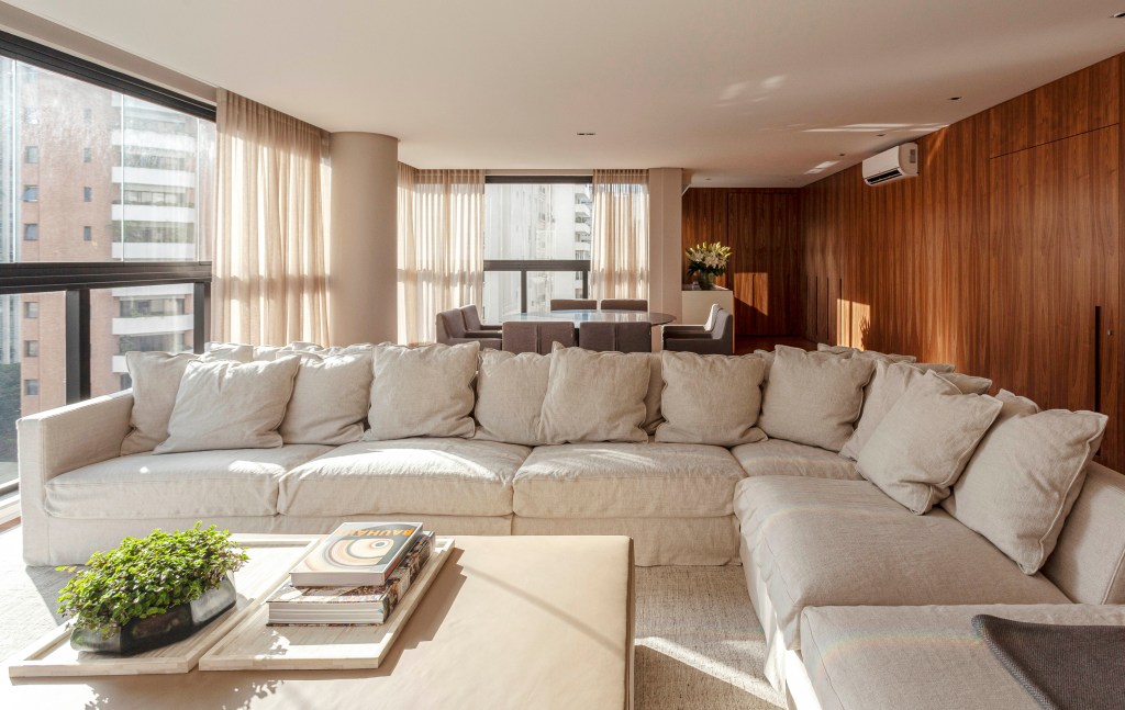 David Bastos assina apartamento clássico de 174 m² em São Paulo. Na foto, sala de estar e de jantar com paredes de madeira e quadros,