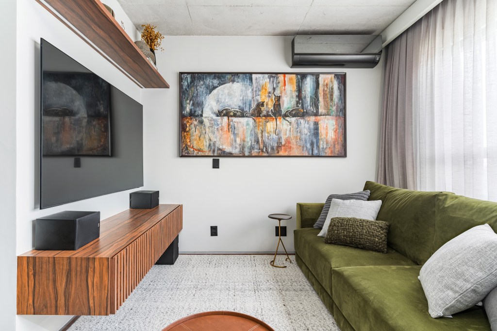 Gabriela Prado assina apê industrial de 140 m² com jardim de cactos. Na foto, sala de TV com quadro e sofá verde.