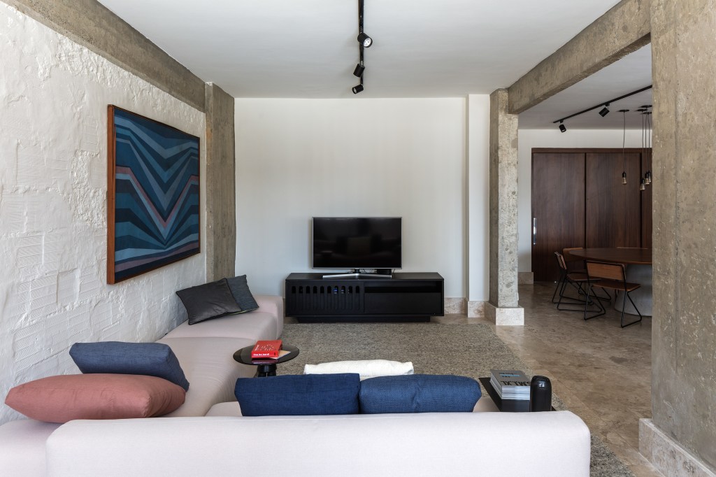 José Navarro assina apartamento de 210 m² no Conjunto Nacional, em SP. Na foto, sala de TV com quadros e paredes de concreto.