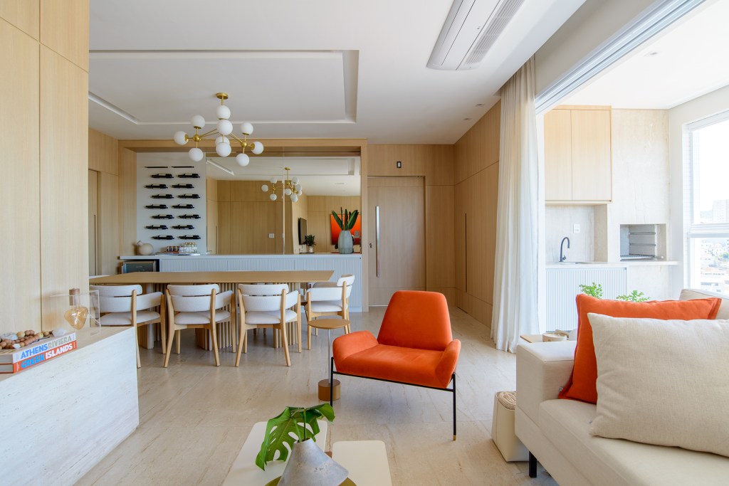 Móveis contemporâneos e paredes amadeiradas marcam este apê de 138 m². Projeto de Leticia Nanetti. Na foto, sala de estar com sofá branco e quadro laranja. Sala de jantar e adega.