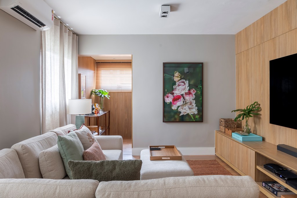 Paola Ribeiro assina apartamento de 196 m² com alma carioca em SP. Projeto de Paola Ribeiro, Na foto, sala de tv com sofá em L branco e quadro.