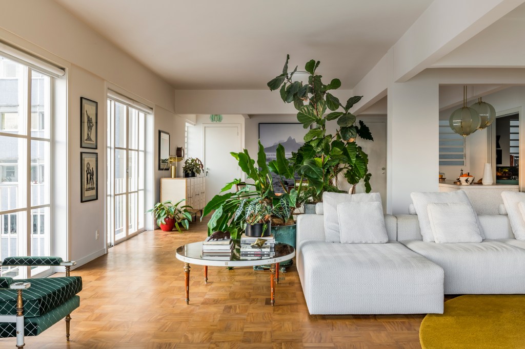 Reforma restaura itens originais em apartamento do Edifício Saint Honoré. Projeto Sao Arquitetura. Na foto, sala com sofá branco, plantas e piso de madeira,