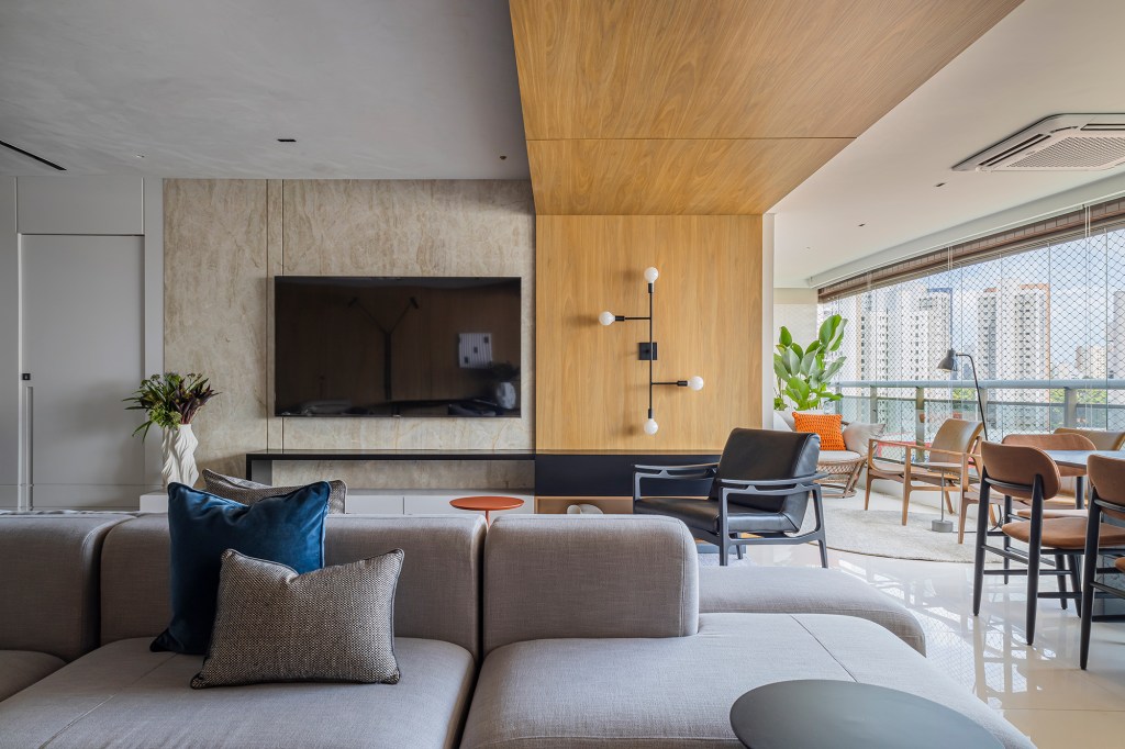 Romário Rodrigues cria projeto contemporâneo em apê de 220 m² no Ceará. Na foto, sala de estar e varanda com pórtico de madeira e tv.