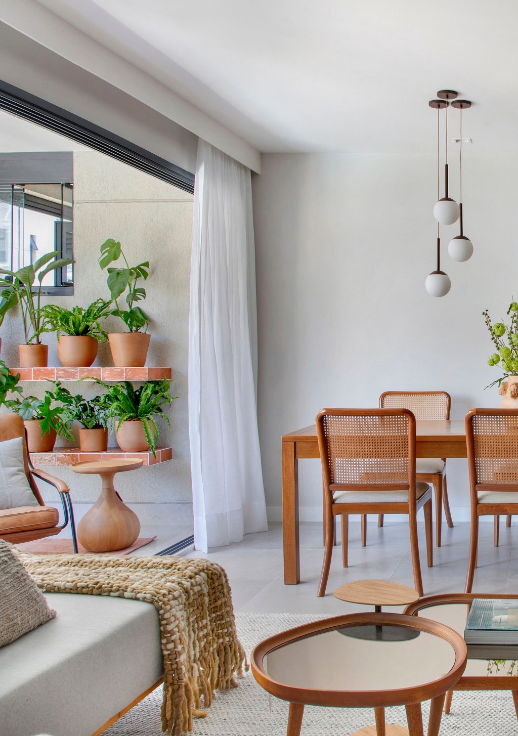 Sem quebra-quebra, apê de 92 m² ganha projeto afetivo e com biofilia. Projeto de Fabiano Ravaglia. Na foto, sala de jantar com varanda, vasos e sofá.