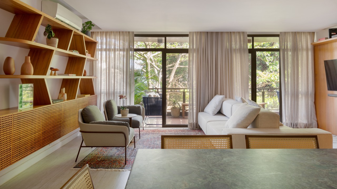 A madeira é a protagonista deste apartamento de 117 m² na Gávea. Projeto de Mariana Monnerat, Na foto, sala com estante assimétrica de madeira. Varanda e sofá ilha.