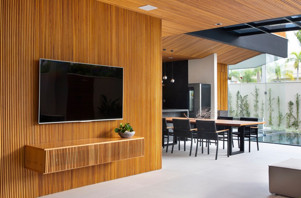 Painéis de madeira e estilo minimalista dão o tom desta casa de 780 m². Projeto de Hannah Cabral e Monique Pampolha. Na foto, sala de estra com tv e sala de jantar.