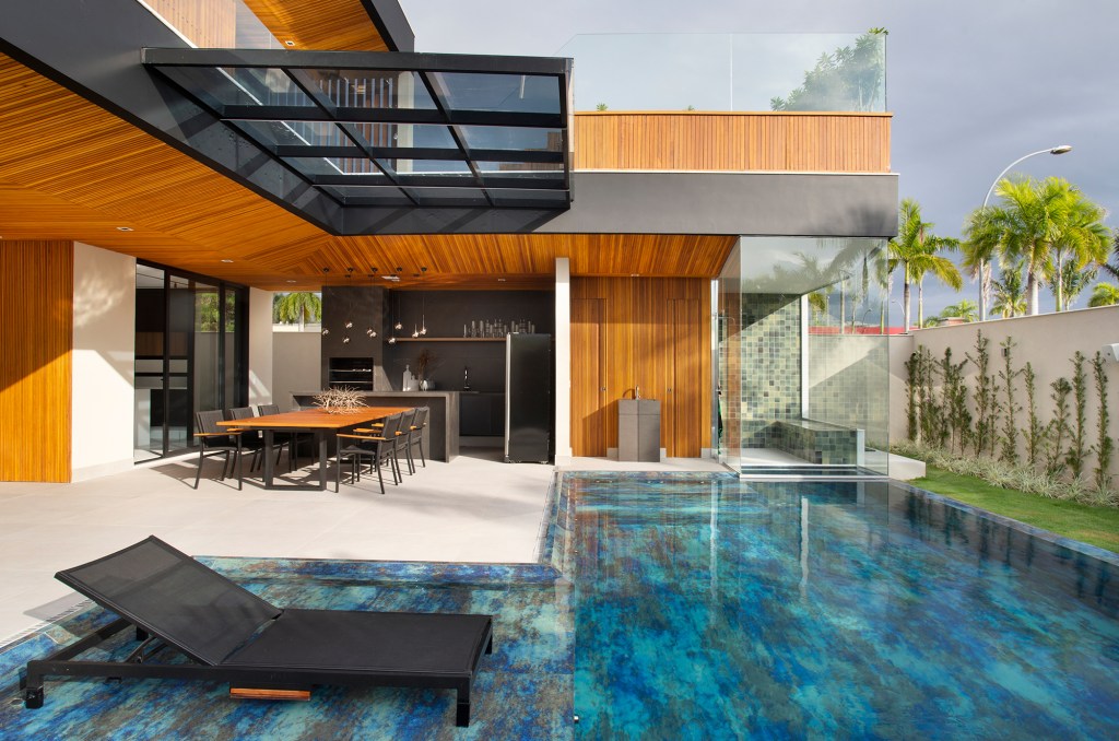 Painéis de madeira e estilo minimalista dão o tom desta casa de 780 m². Projeto de Hannah Cabral e Monique Pampolha. Na foto, varanda gourmet com piscina e churrasqueira,