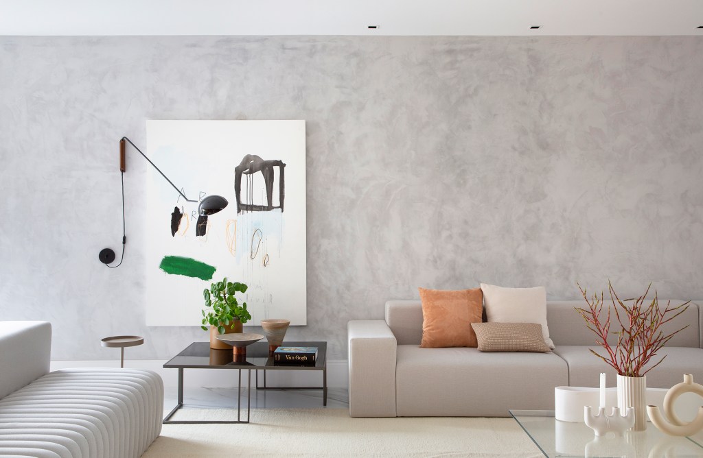 Painéis de madeira e estilo minimalista dão o tom desta casa de 780 m². Projeto de Hannah Cabral e Monique Pampolha. Na foto, sala com escada, parede ripada e sofá branco.