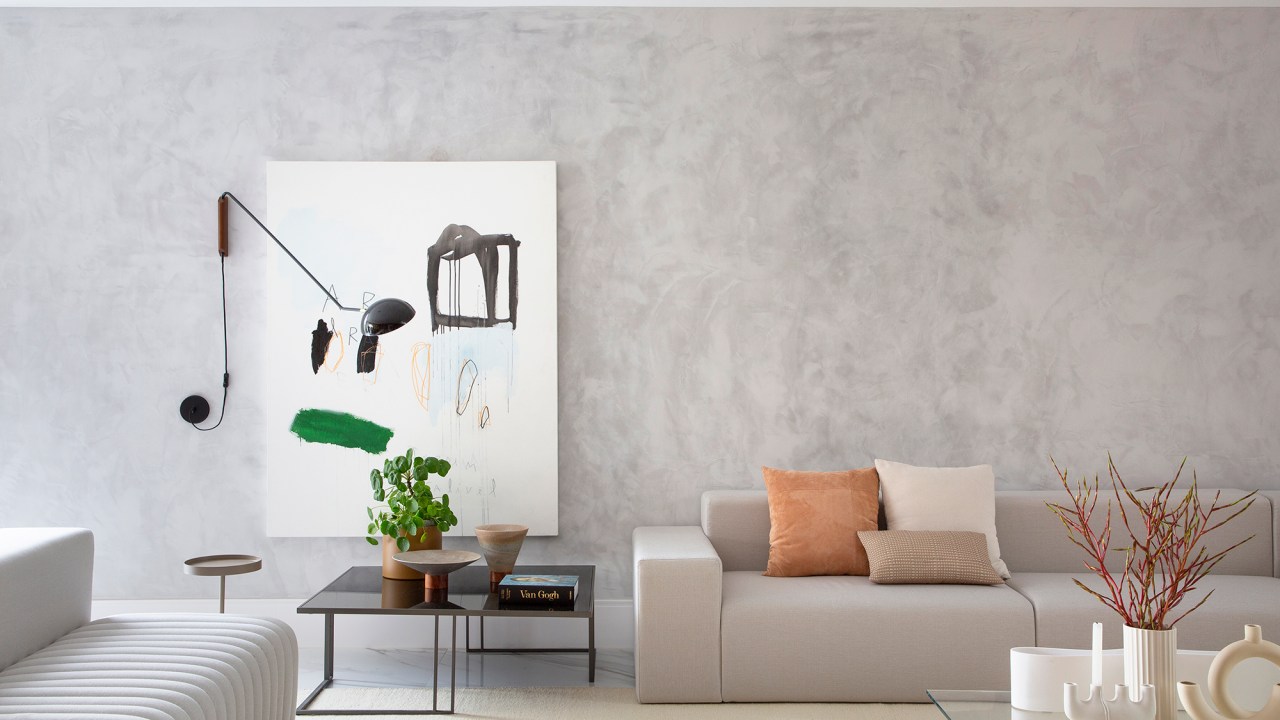 Painéis de madeira e estilo minimalista dão o tom desta casa de 780 m². Projeto de Hannah Cabral e Monique Pampolha. Na foto, sala com escada, parede ripada e sofá branco.