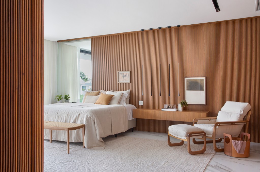 Painéis de madeira e estilo minimalista dão o tom desta casa de 780 m². Projeto de Hannah Cabral e Monique Pampolha. Na foto, quarto de casal com parede ripada e poltrona.