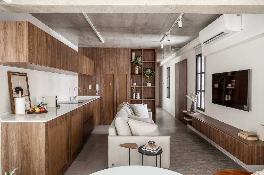 Wabi-sabi norteia a decoração de apartamento de apenas 48 m². Projeto de Carolina Gava. Na foto. sala com sofá branco e cozinha integrada.