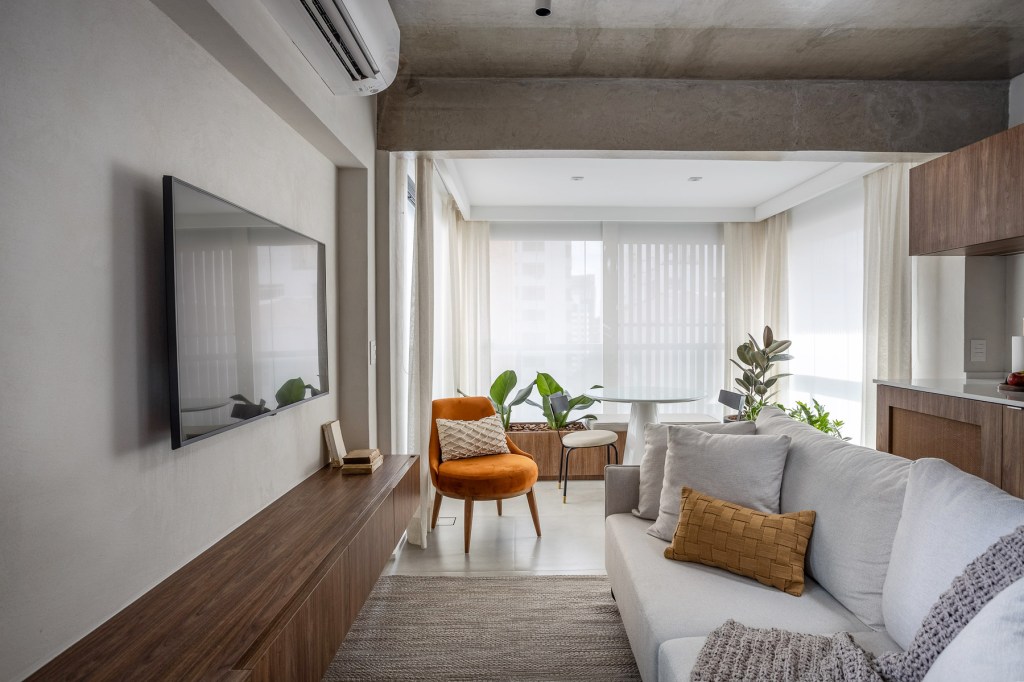 Wabi-sabi norteia a decoração de apartamento de apenas 48 m². Projeto de Carolina Gava. Na foto. sala de estar com sofá branco, cozinha e tv,