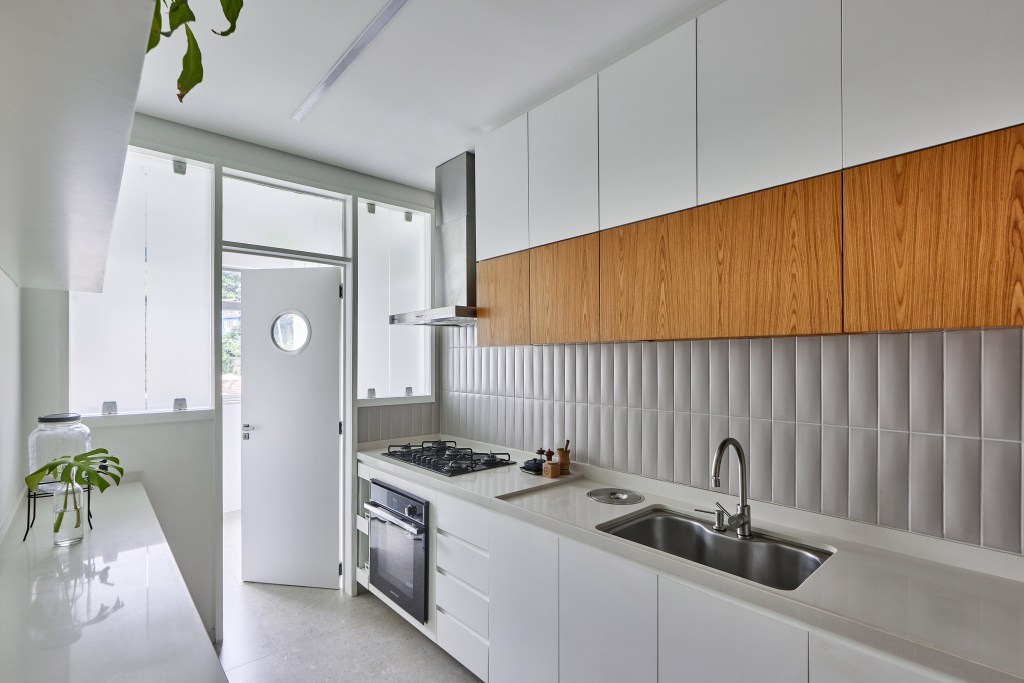 Apartamento de 98 m² ganha décor contemporâneo, mas com toques de brutalismo. Projeto de Hugo Rapizo. Na foto, cozinha corredor com marcenaria branca.