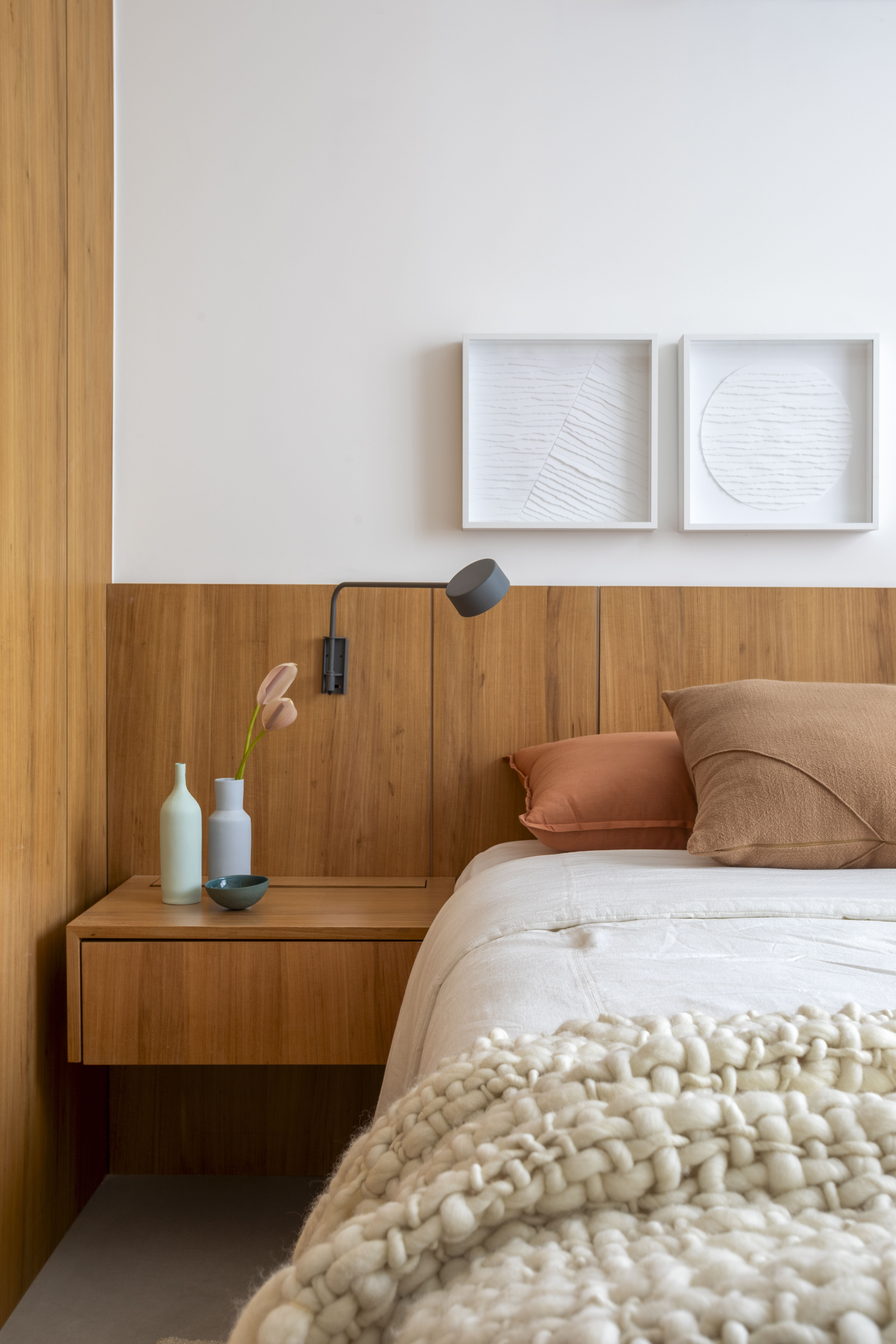 Branco e madeira criam décor cozy em apartamento de 70 m². Projeto de Rafael Ramos. Na foto, quarto de casal com cabeceira de madeira e quadros.