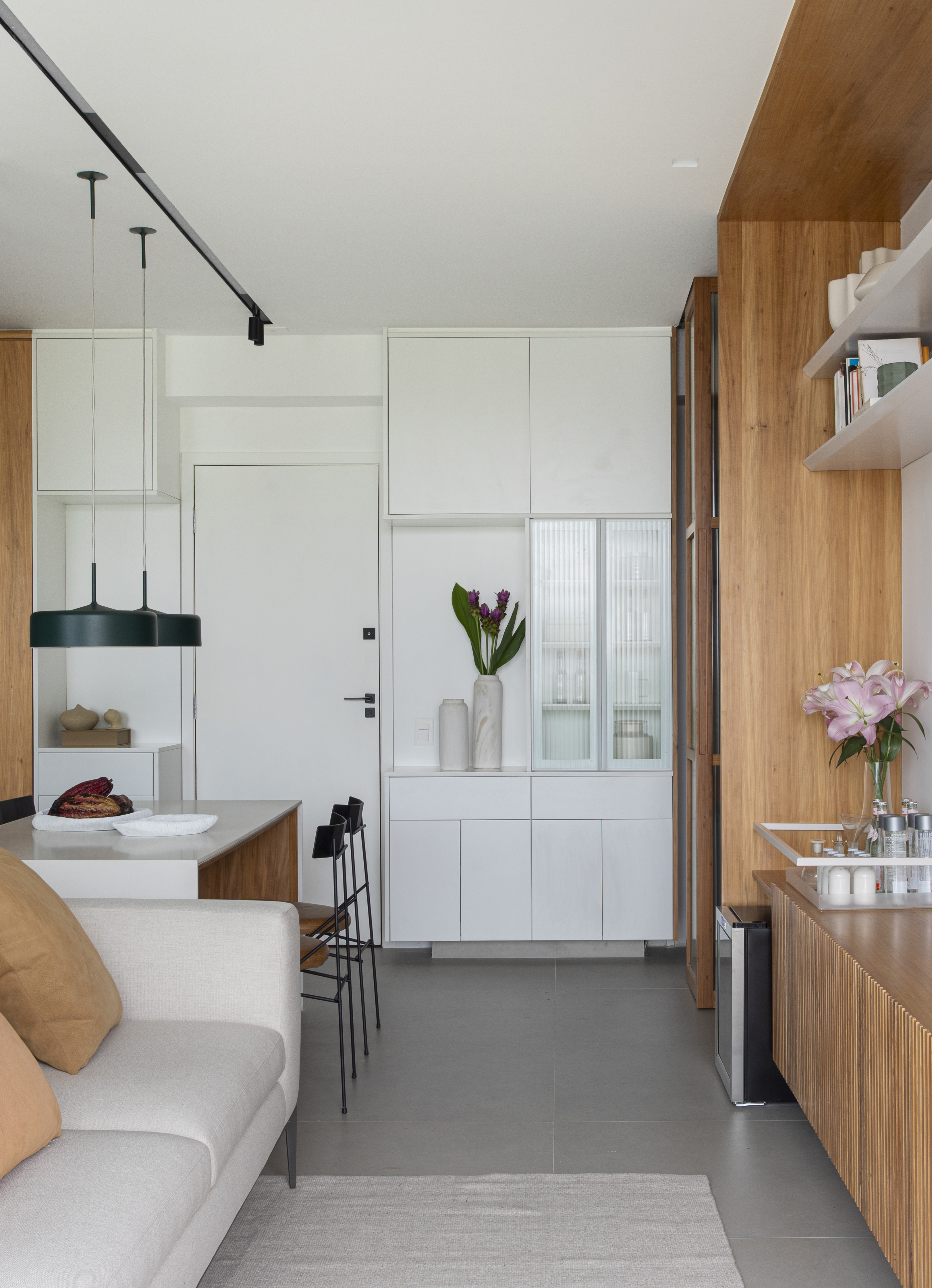 Branco e madeira criam décor cozy em apartamento de 70 m². Projeto de Rafael Ramos. Na foto, sala de tv com aparador ripado e prateleiras. Cozinha integrada.
