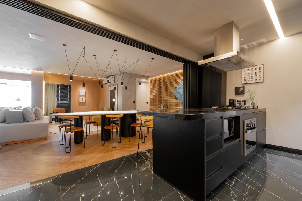 Cores escuras criam sobriedade neste apartamento de 100 m². Projeto de Romário Rodrigues. Na foto, cozinha aberta com decoração preta. Sala de jantar integrada com parede de muxarabi.