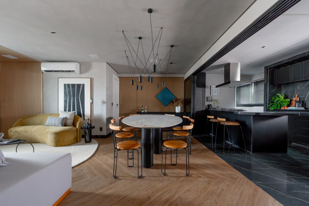 Cores escuras criam sobriedade neste apartamento de 100 m². Projeto de Romário Rodrigues. Na foto, sala de jantar com parede de muxarabi, mesa oval e cozinha integrada.