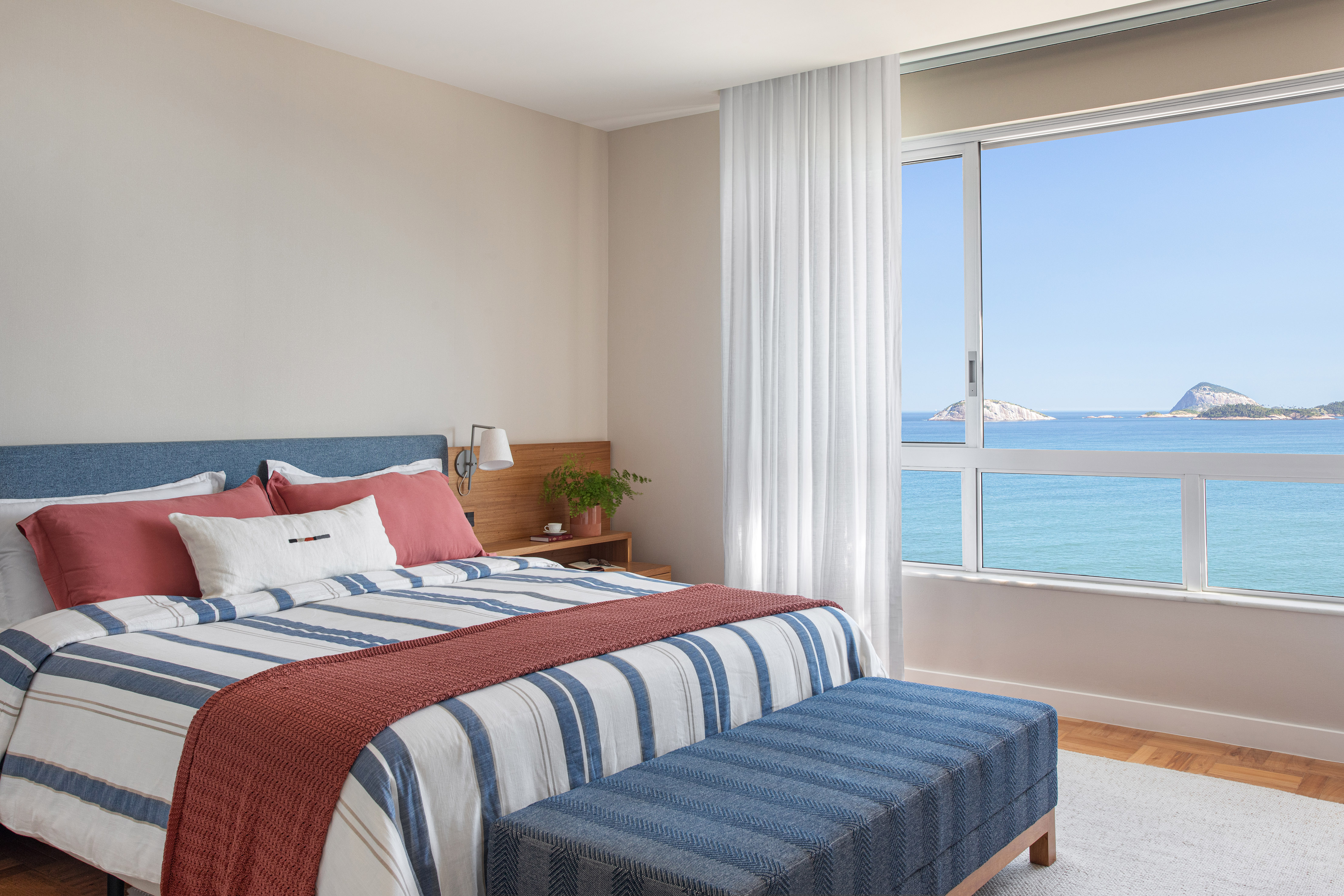Marcenaria multifuncional caracteriza apartamento com vista para o Cristo. Projeto de Escala Arquitetura. Na foto, quarto de casal com cabeceira azul e vista para o mar.