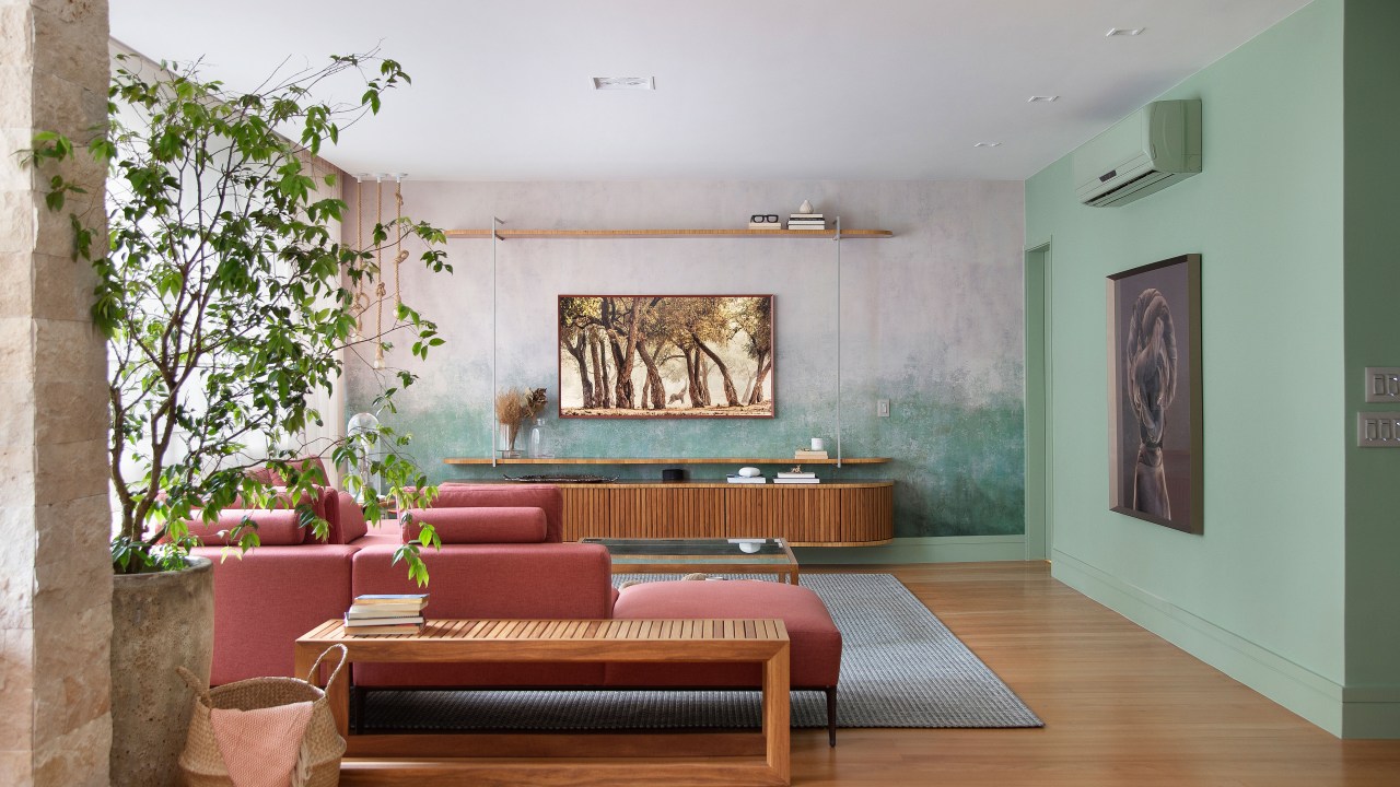 Papel de parede com efeito degradê envelhecido é destaque deste apê. Projeto de Manoela Fleck. Na foto, sala de estar com sofá terracota, banco e vaso.