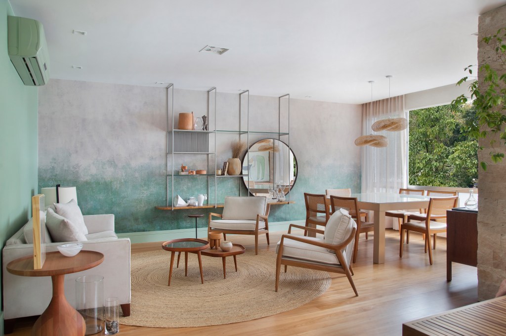 Papel de parede com efeito degradê envelhecido é destaque deste apê. Projeto de Manoela Fleck. Na foto, sala de estar e jantar com mesa, estante e sofá.