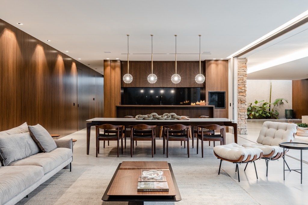 Tons escuros e grandes aberturas criam sofisticação em casa de 430 m². Projeto de Aline Borges. Na foto, sala com painel de madeira e mesa de jantar.
