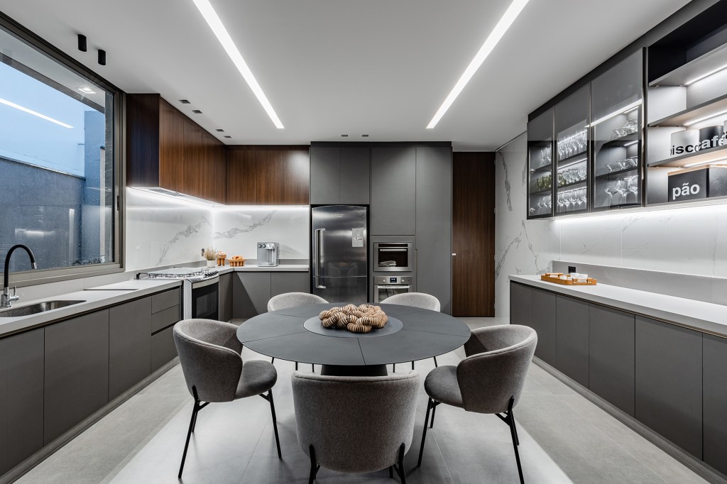 Tons escuros e grandes aberturas criam sofisticação em casa de 430 m². Projeto de Aline Borges. Na foto, sala de jantar com cozinha e cristaleira.