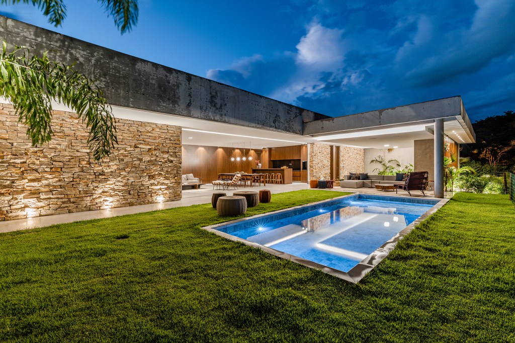 Tons escuros e grandes aberturas criam sofisticação em casa de 430 m². Projeto de Aline Borges. Na foto, jardim com piscina e fachada.